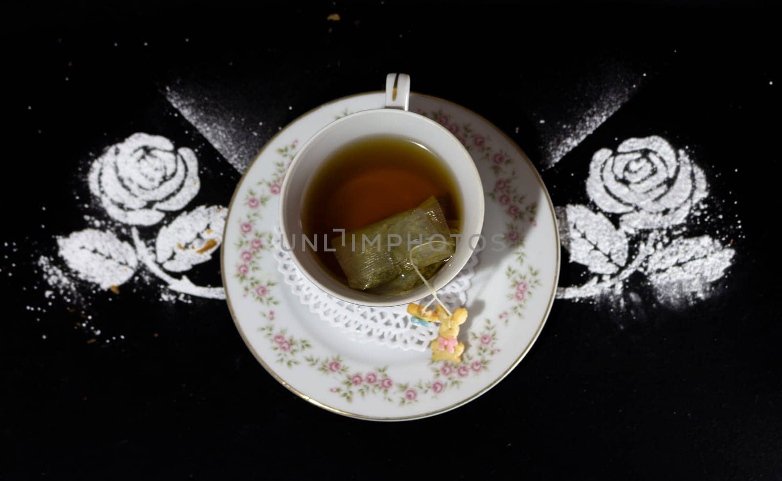 Antique porcelain tea cup seen from above with flowers, the tea bag inside and a small doll of candy growing, decorated with two powdered sugar flowers. High quality photo