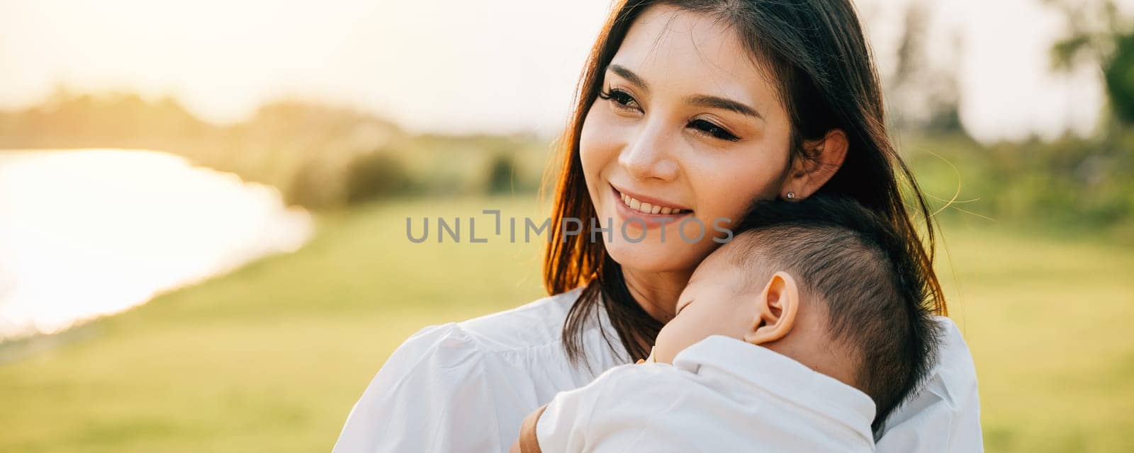Family care. Happy beautiful mother holding baby sleeping son in the park at evening time before sunset, Portrait of mom hold newborn feeling happy and smiles in the garden nature outdoor, Mother Day