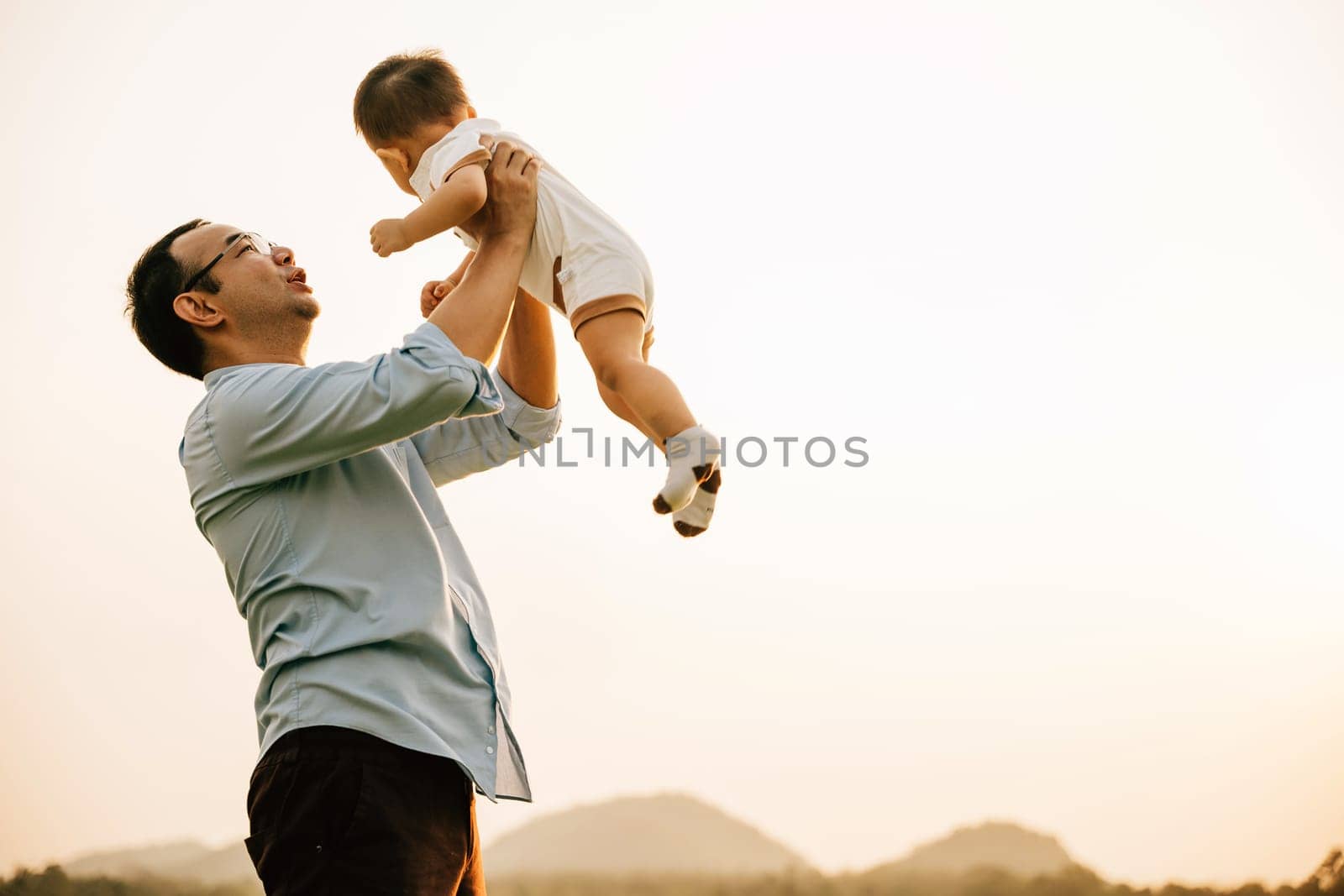 Father holds his baby daughter up high throwing up by Sorapop