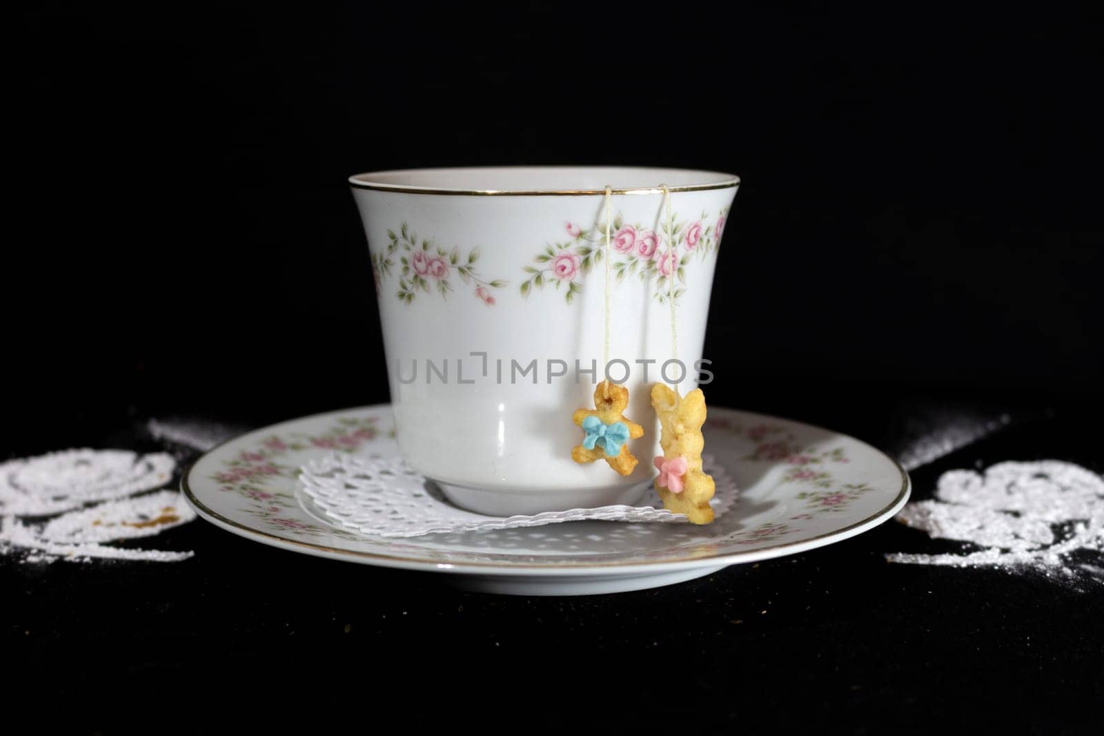 Classic cup of tea surrounded by two white roses made with icing sugar and a rabbit-shaped sweet that hangs over the cup. High quality photo