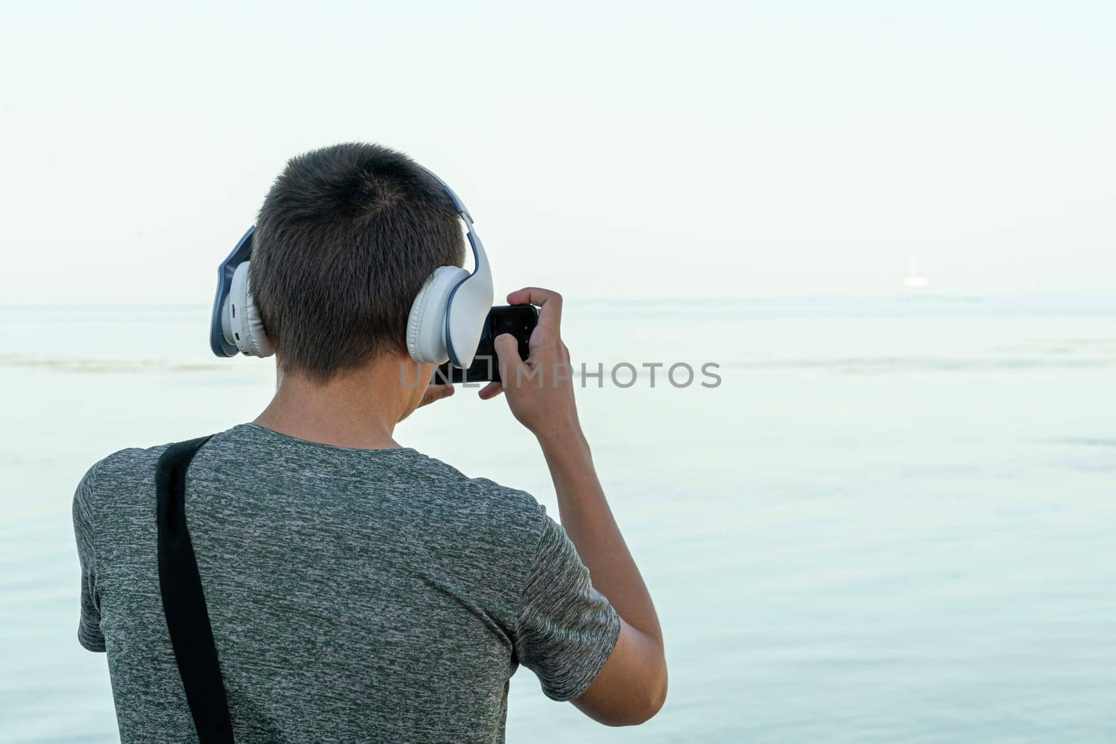 a young man takes pictures on his phone on the seashore by roman112007