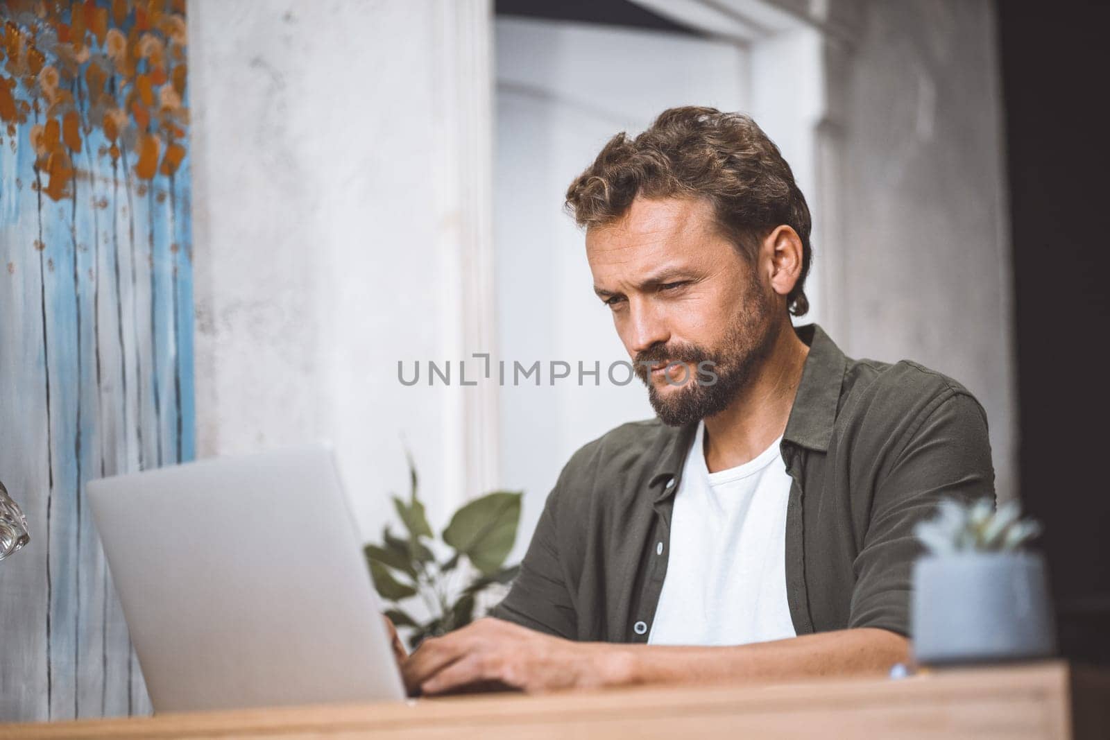 Man is working from home, focused on laptop while sitting at desk in home office. He freelancer or digital nomad, taking advantage of flexibility that remote work provides. Idea of productive remote work, with man being concentrated and productive while enjoying the comfort of own home. High quality photo