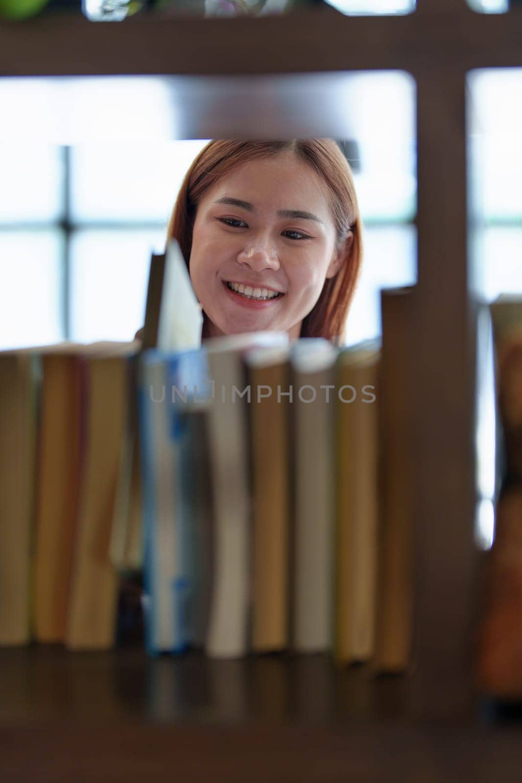 Portrait of a young Asian woman showing joy as she searches for knowledge in the library by Manastrong