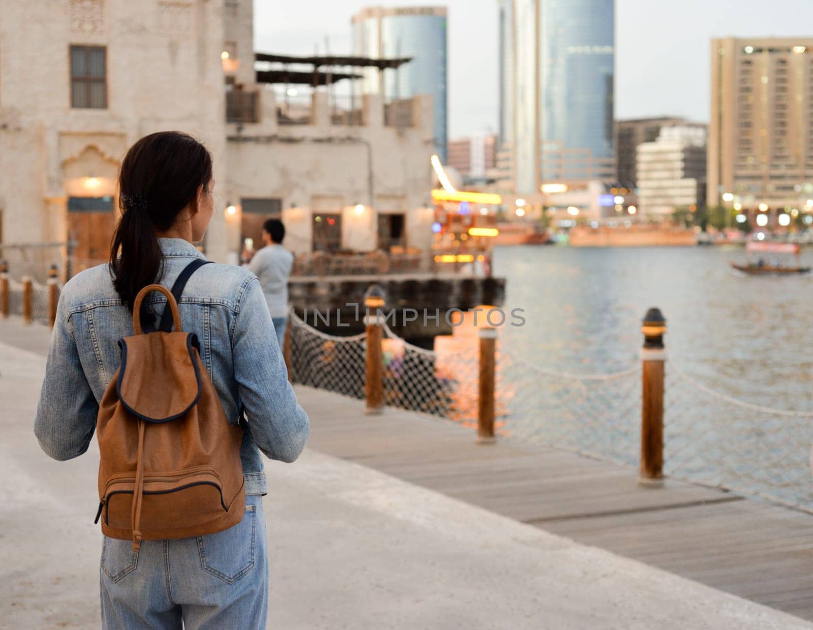 A young woman with a backpack on her back admires the river in the old Dubai Creek. Back view. Journey through the Persian Gulf by Ekaterina34