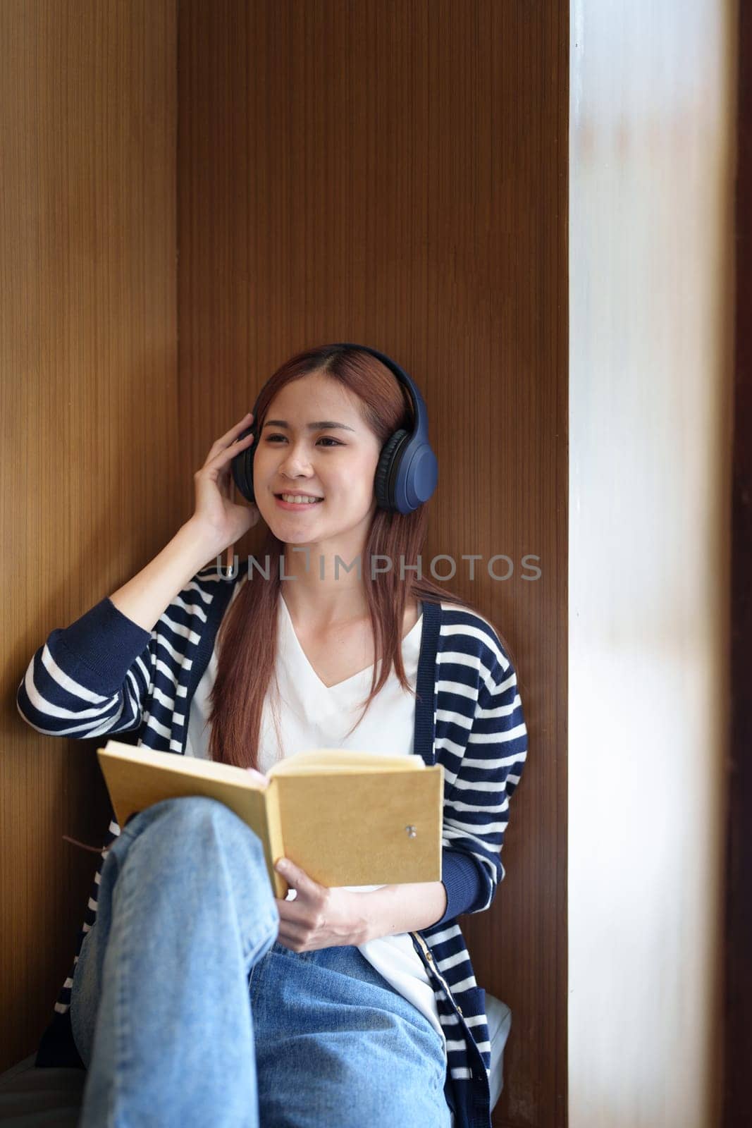 Portrait of a loving Asian teenage girl wearing headphones using a notebook while listening to an online lesson by Manastrong