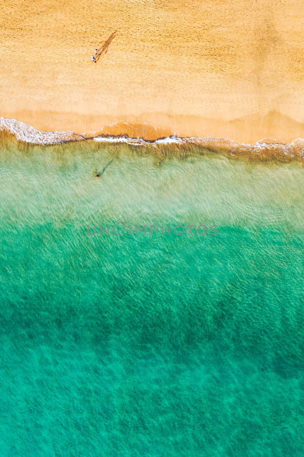 Aerial view of the walking people on the white sandy beach near sea with waves at sunset. Summer holiday. Top view of sporty people, clear azure water. Lifestyle and sport