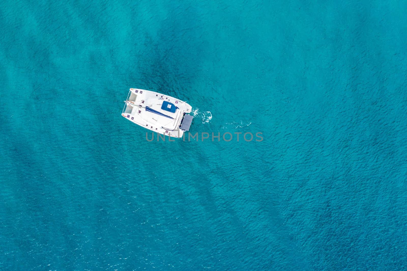 Aerial view of anchored sailing yacht in emerald sea. Aerial view of a boat. Outdoor water sports, yachting. Aerial view of anchoring yacht in open water. Ocean and sea travel and transportation