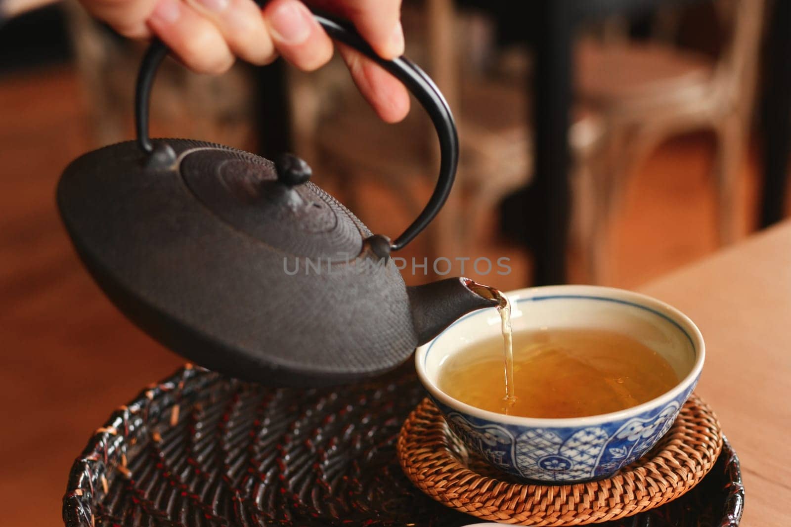 Hand pours green tea from a cast iron teapot into a cap