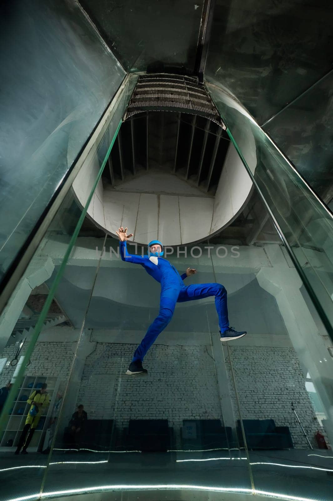 A man in overalls and a protective helmet enjoys flying in a wind tunnel. Free fall simulator by mrwed54