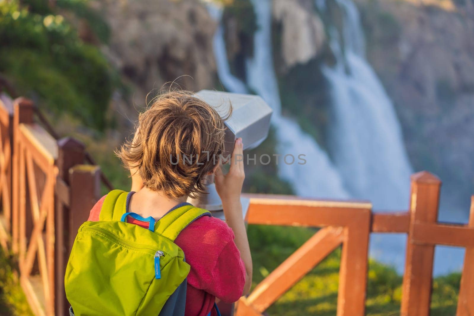 Boy tourist with a backpack on the background of Duden waterfall in Antalya. Famous places of Turkey. Lower Duden Falls drop off a rocky cliff falling from about 40 m into the Mediterranean Sea in amazing water clouds. Tourism and travel destination photo in Antalya, Turkey. Turkiye.