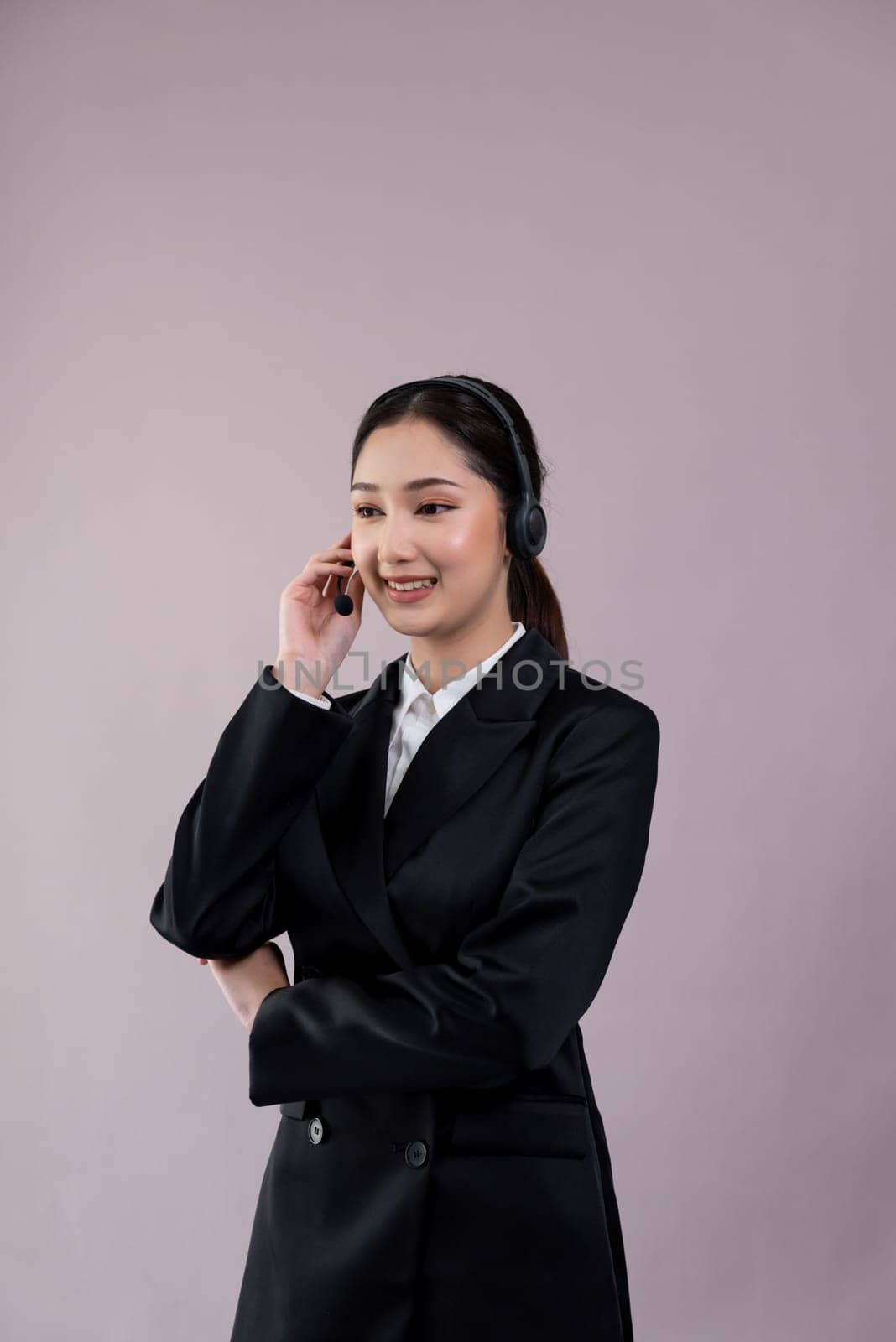 Attractive asian female call center operator with happy smile face advertises job opportunity on empty space, wearing a formal suit and headset on customizable isolated background. Enthusiastic