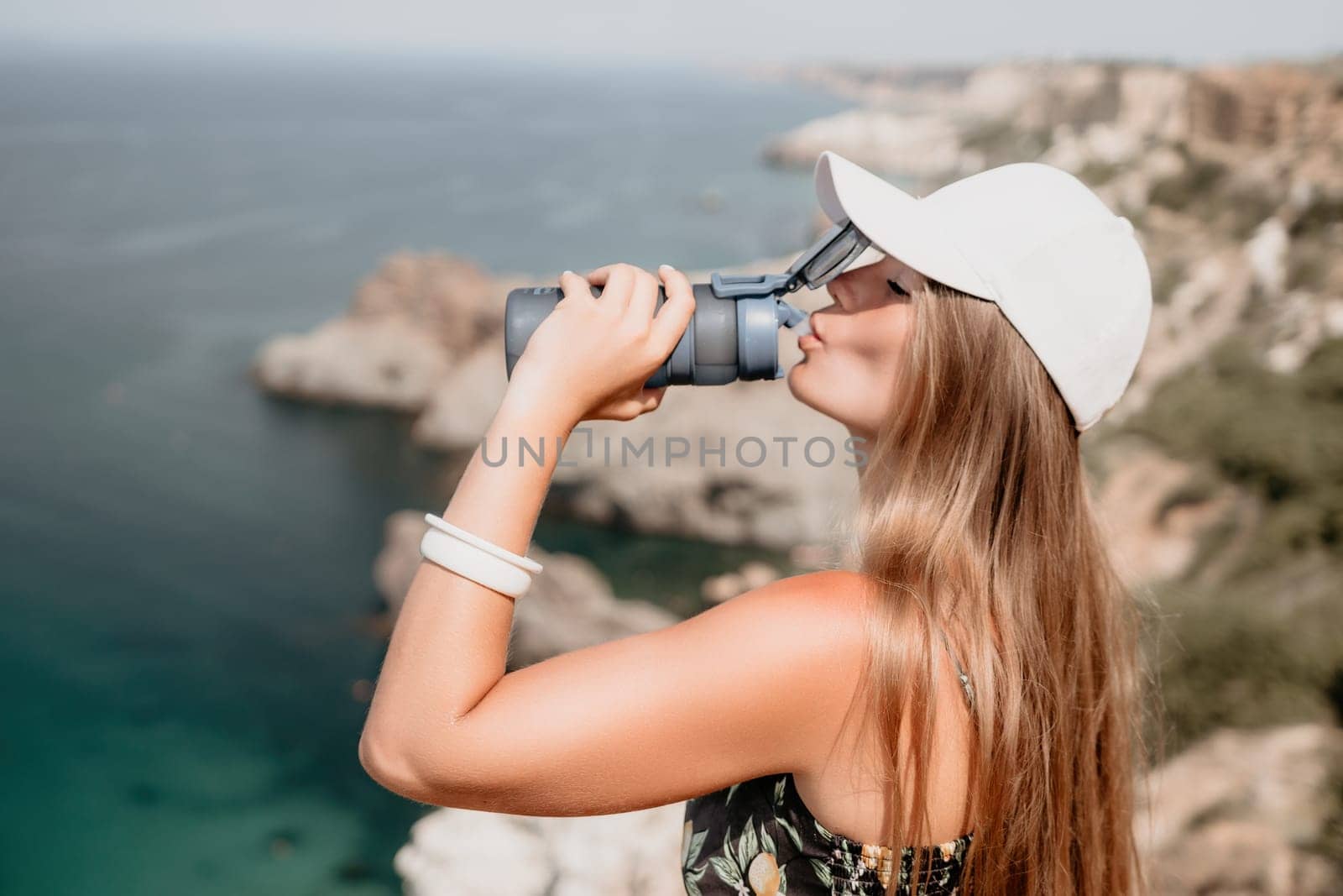 Woman travel sea. Happy tourist drink water on hot summer day. Woman traveler looks at the edge of the cliff on the sea bay of mountains, sharing travel adventure journey by panophotograph