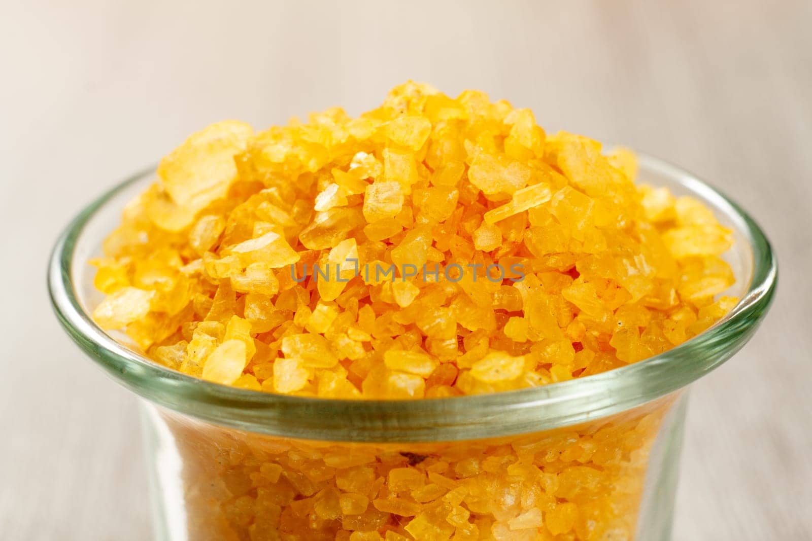 Close-up glass bowl with yellow sea salt for bathroom procedures. Spa products and accessories. Selective focus on salt.