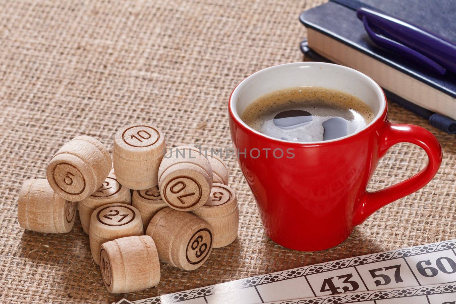 Board game lotto on sackcloth. Wooden lotto barrels and game cards for a game in lotto with cup of coffee and notebook with pen on the background.