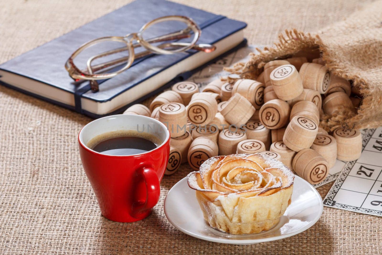 Wooden lotto barrels in bag and game cards with notebook, glasses, cup of coffee and homemade cookie on plate. by mvg6894