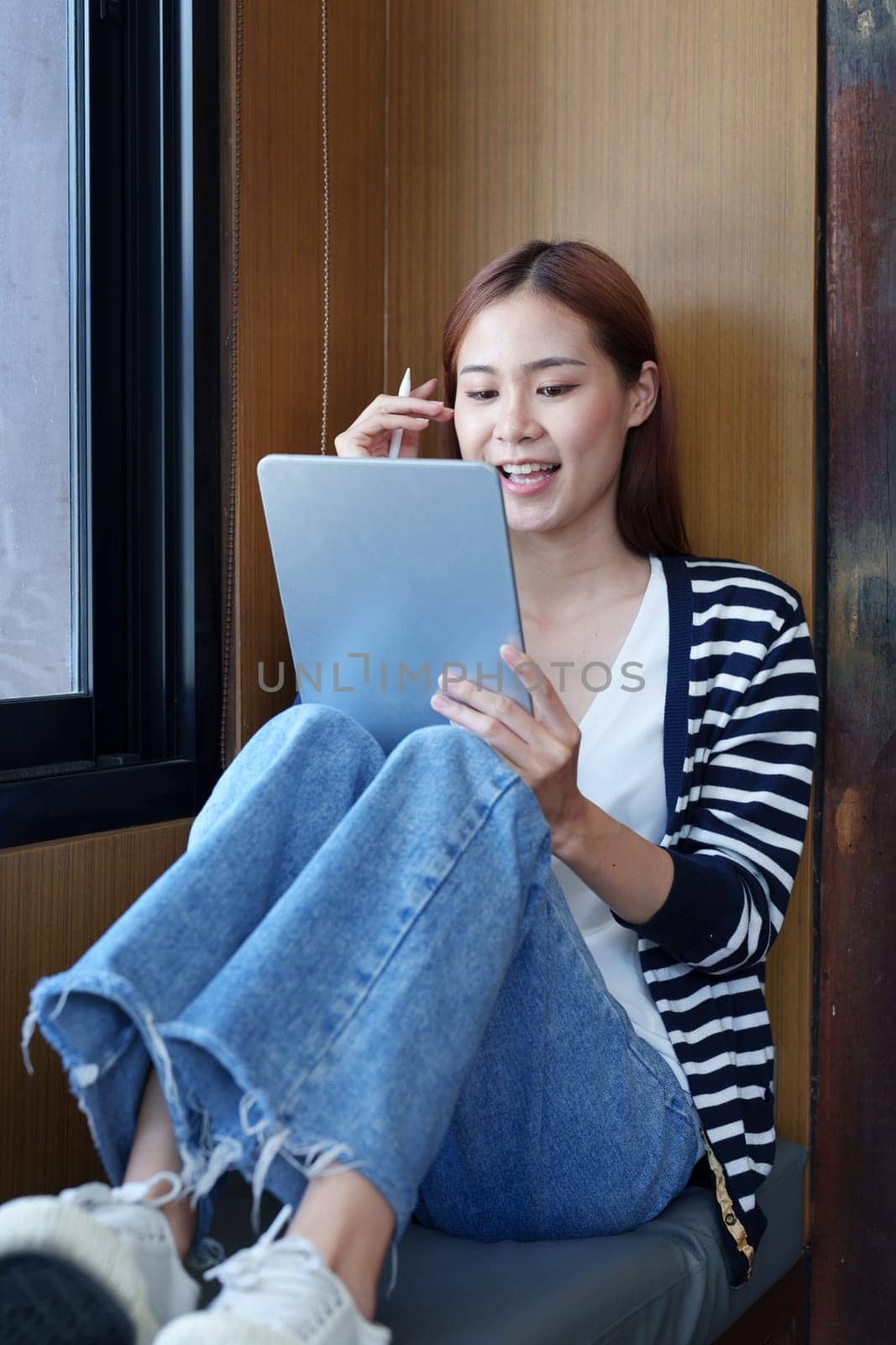 Portrait of a smiling Asian teenage girl using a tablet computer to study online via video conferencing.