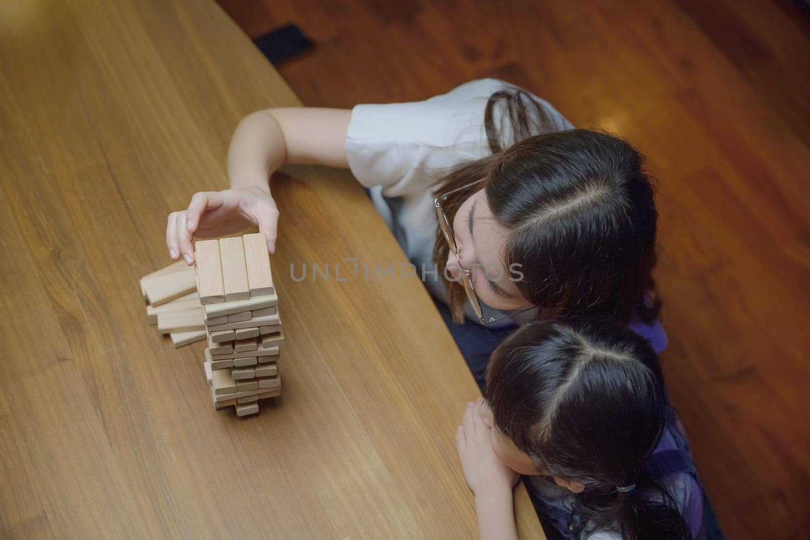 Asian young mother playing game in wood block with her little daughter in home living room by Sorapop