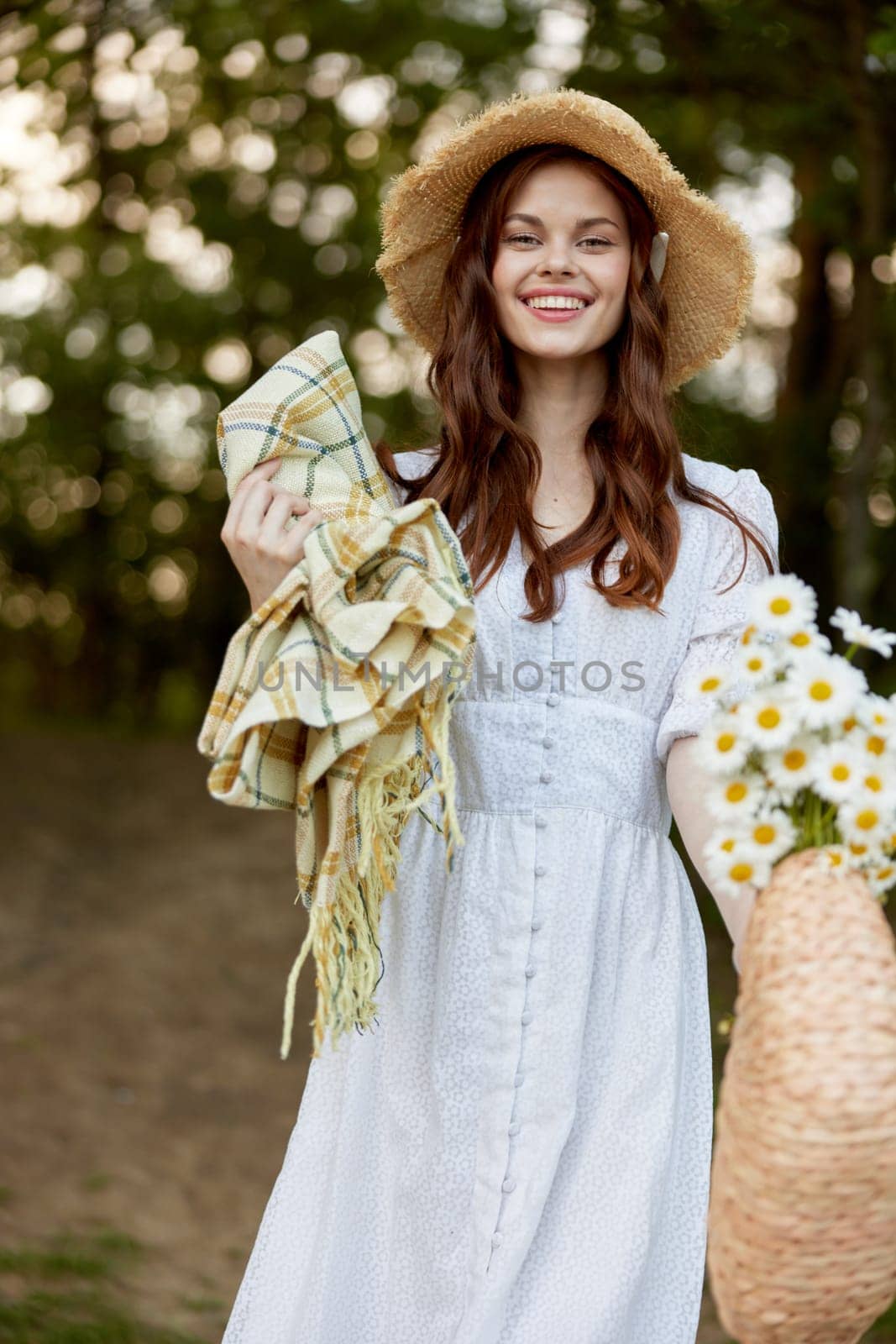 a happy, romantic woman stands in a light dress with a hat on her head and a plaid in her hands in the park. High quality photo