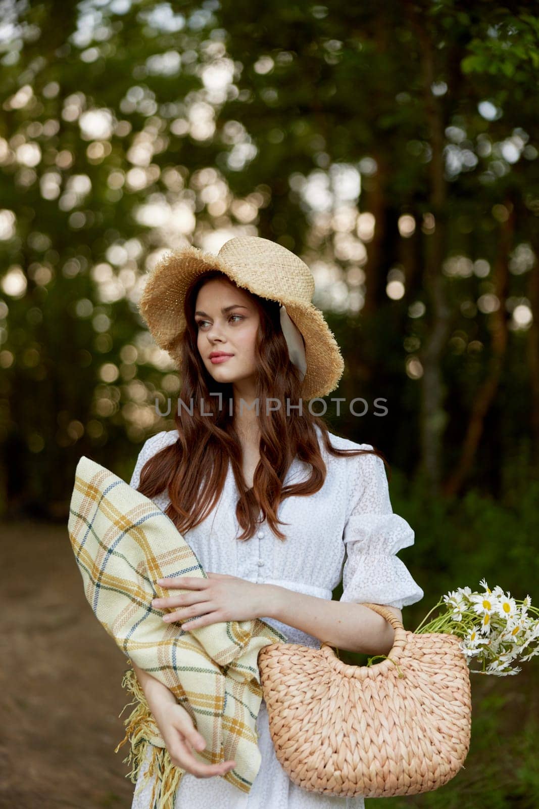 a happy, romantic woman stands in a light dress with a hat on her head and a plaid in her hands in the park. High quality photo