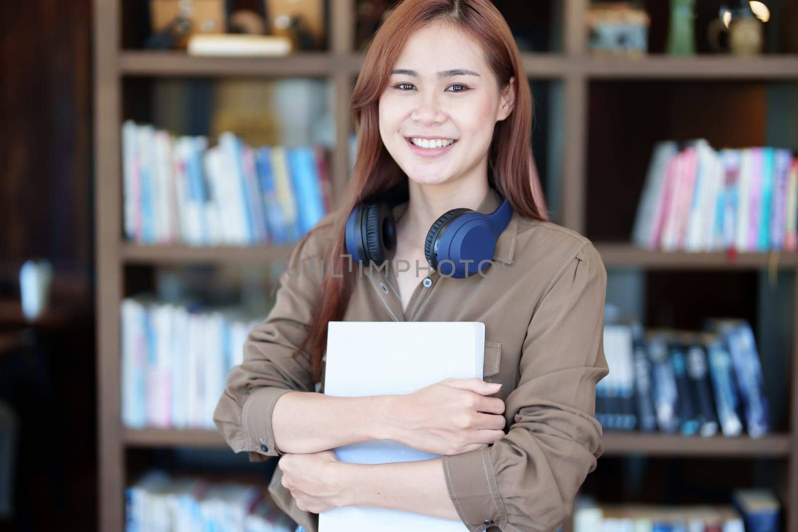 A portrait of a young Asian woman with a smiling face looking for a textbook in the library.