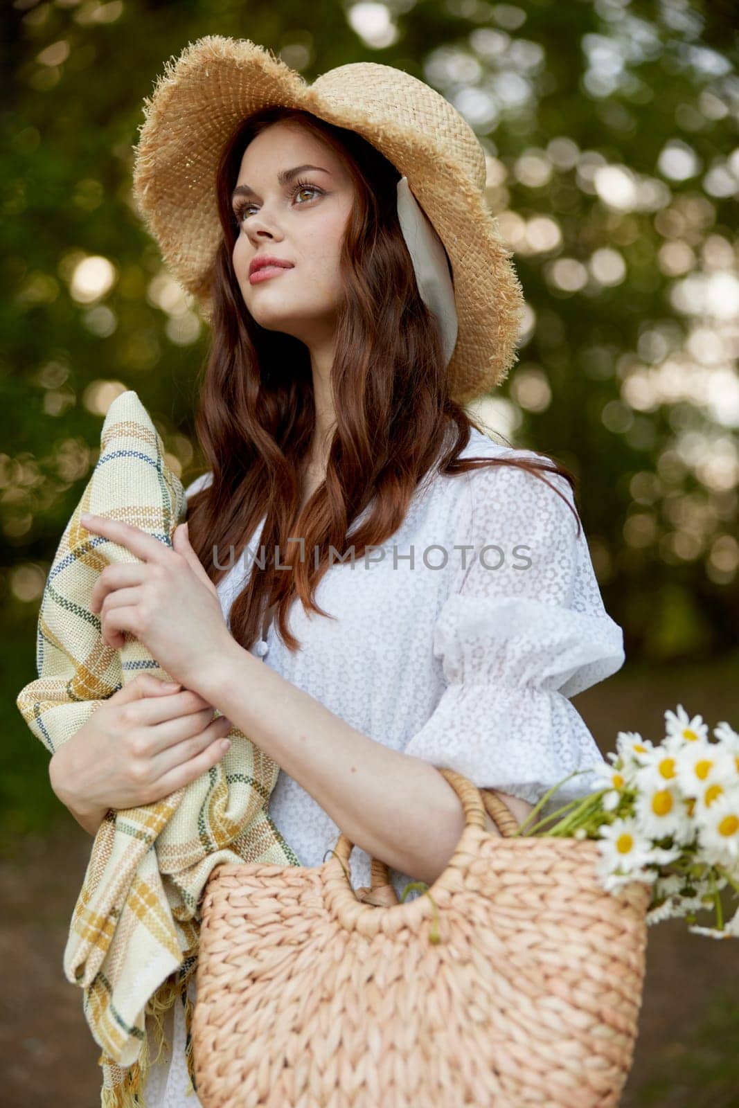 a happy, romantic woman stands in a light dress with a hat on her head and a plaid in her hands in the park. High quality photo