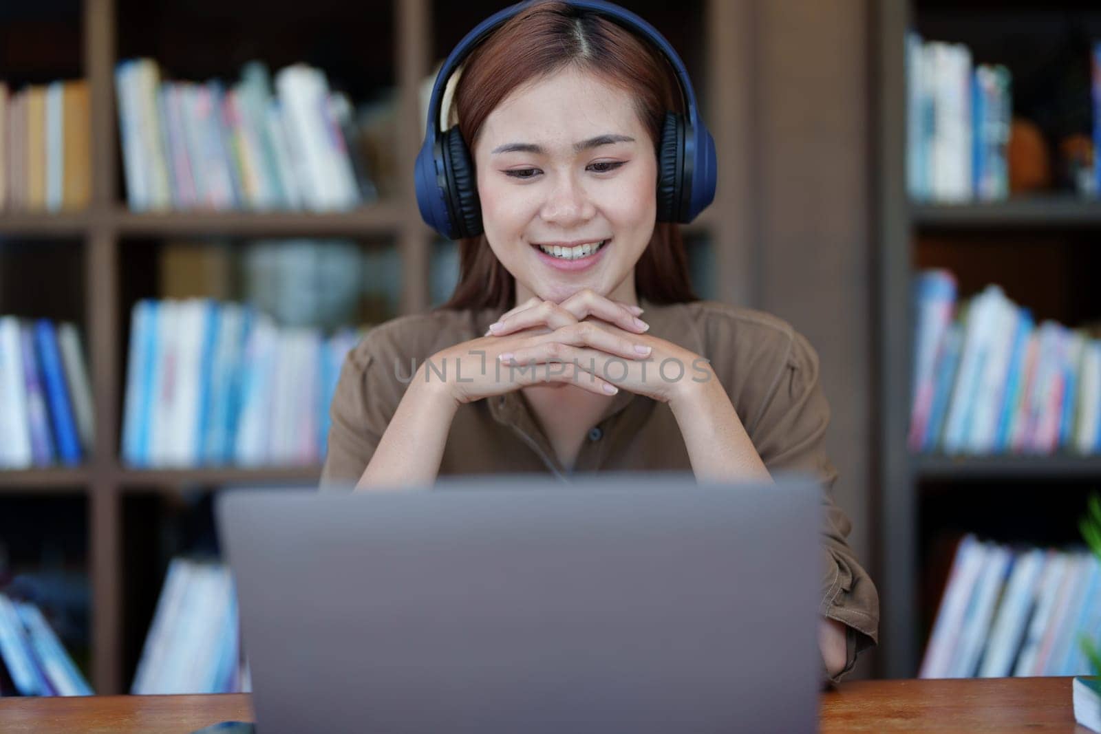 Portrait of a smiling Asian teenage girl wearing headphones and using a computer for online video conferencing in a library.