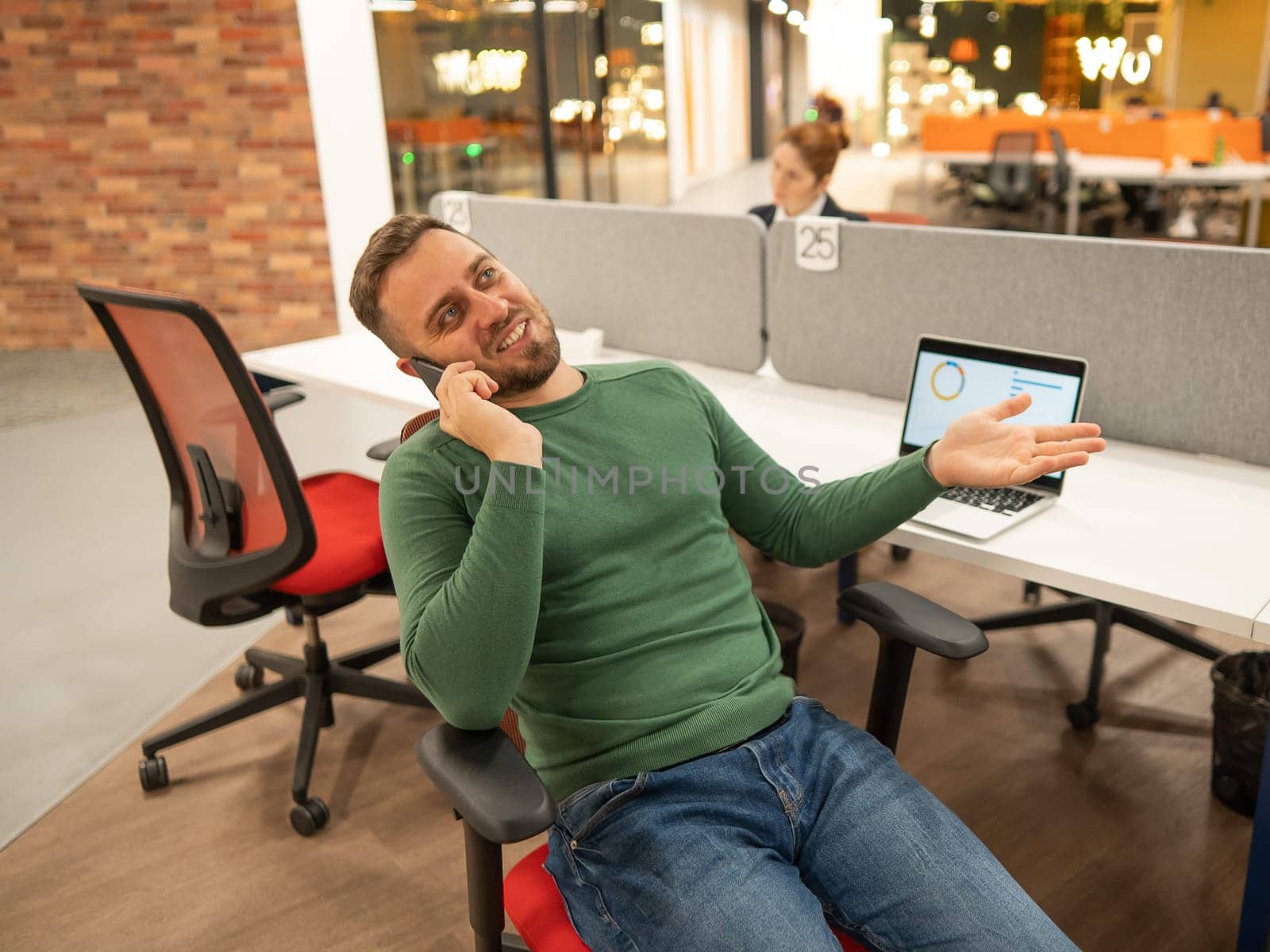 Caucasian bearded man talking on a smartphone while sitting at his desk in a modern coworking space. by mrwed54