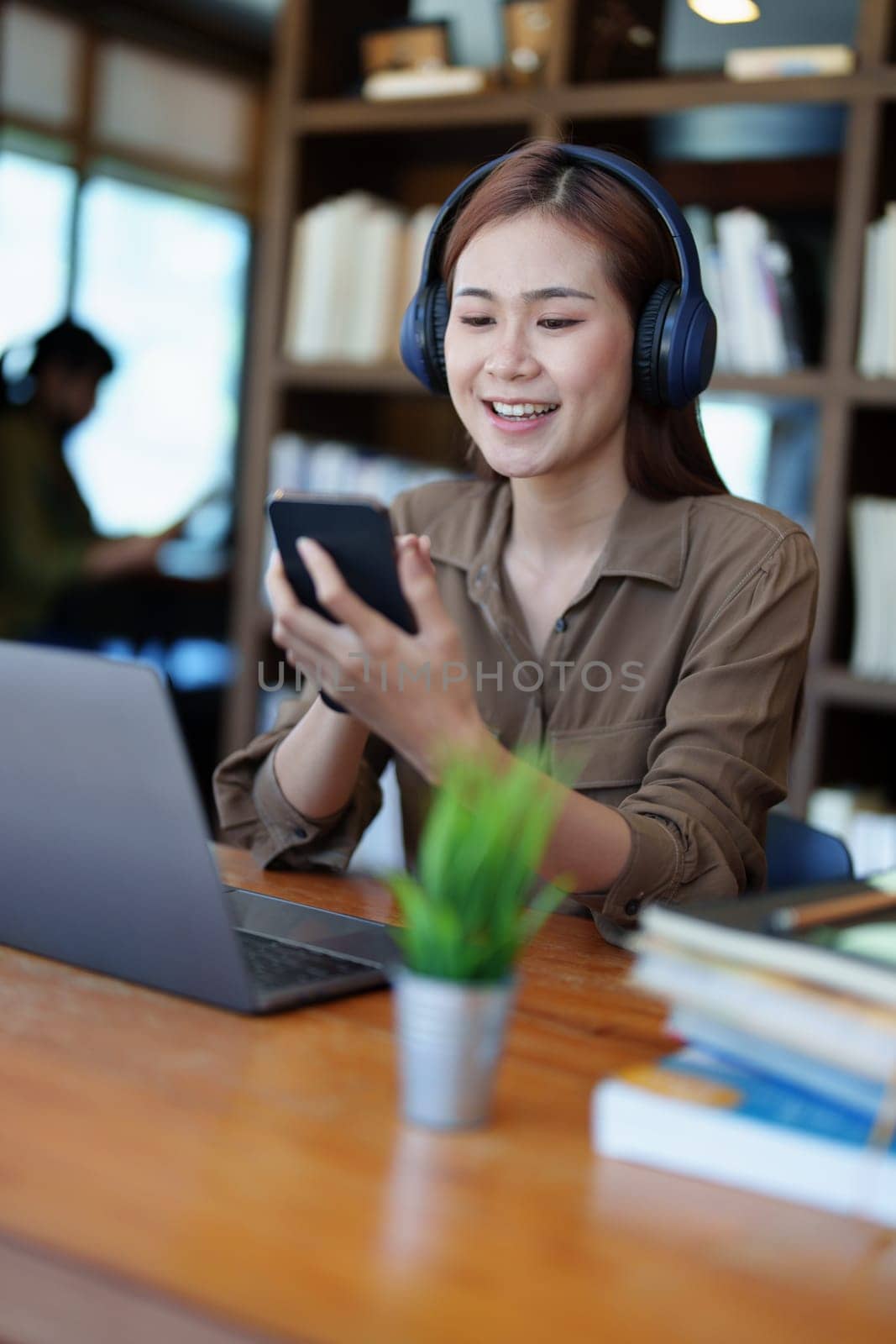 Portrait of a smiling Asian teenage girl wearing headphones and using a computer for online video conferencing in a library.