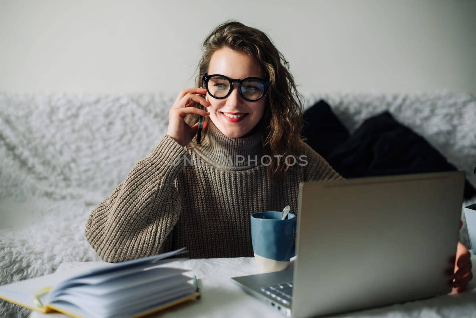 Young accountant manager working at home at the kitchen table, talking on the phone in front of the laptop, smiling, cute talking to CEO or bank support team about corporate account.