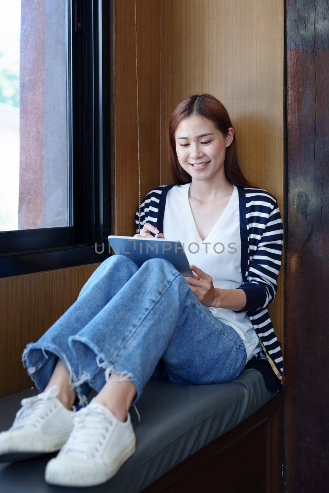 Portrait of a smiling Asian teenage girl using a tablet computer to study online via video conferencing.