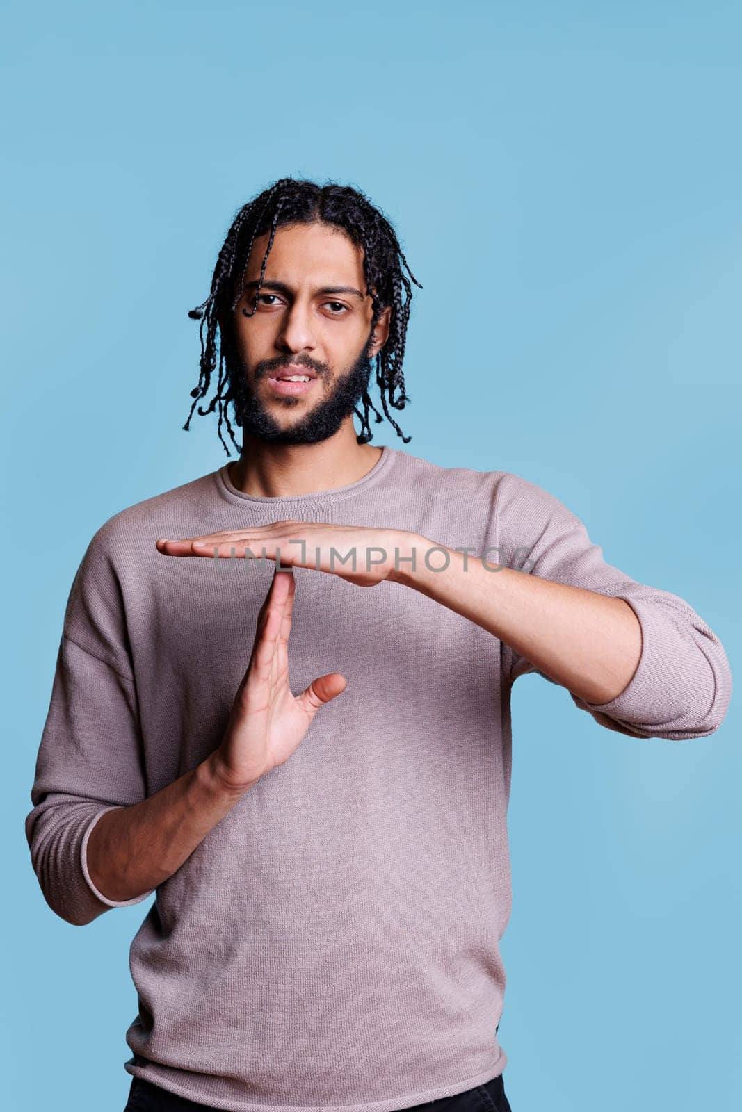 Arab man showing timeout gesture, making pause symbol with hands portrait. Young person doing interruption sign with arms, taking break from communication and looking at camera