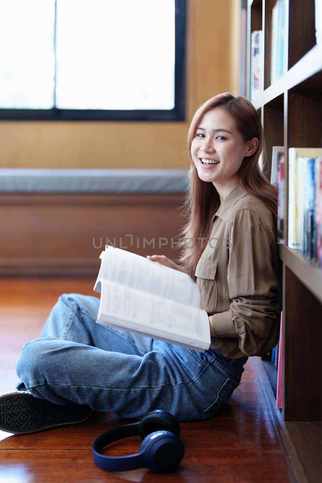 A portrait of a young Asian woman with a smiling face looking for a textbook in the library.