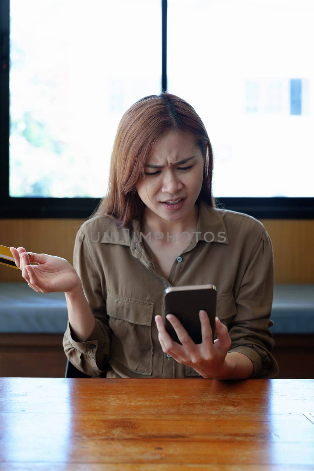 Portrait of a teenage Asian woman expressing dissatisfaction with her credit card being banned while using her phone for online shopping by Manastrong