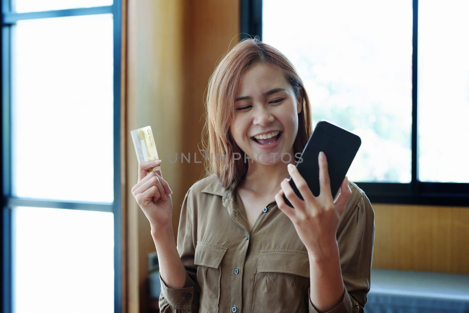 Portrait of young Asian woman using credit card and phone for online shopping.