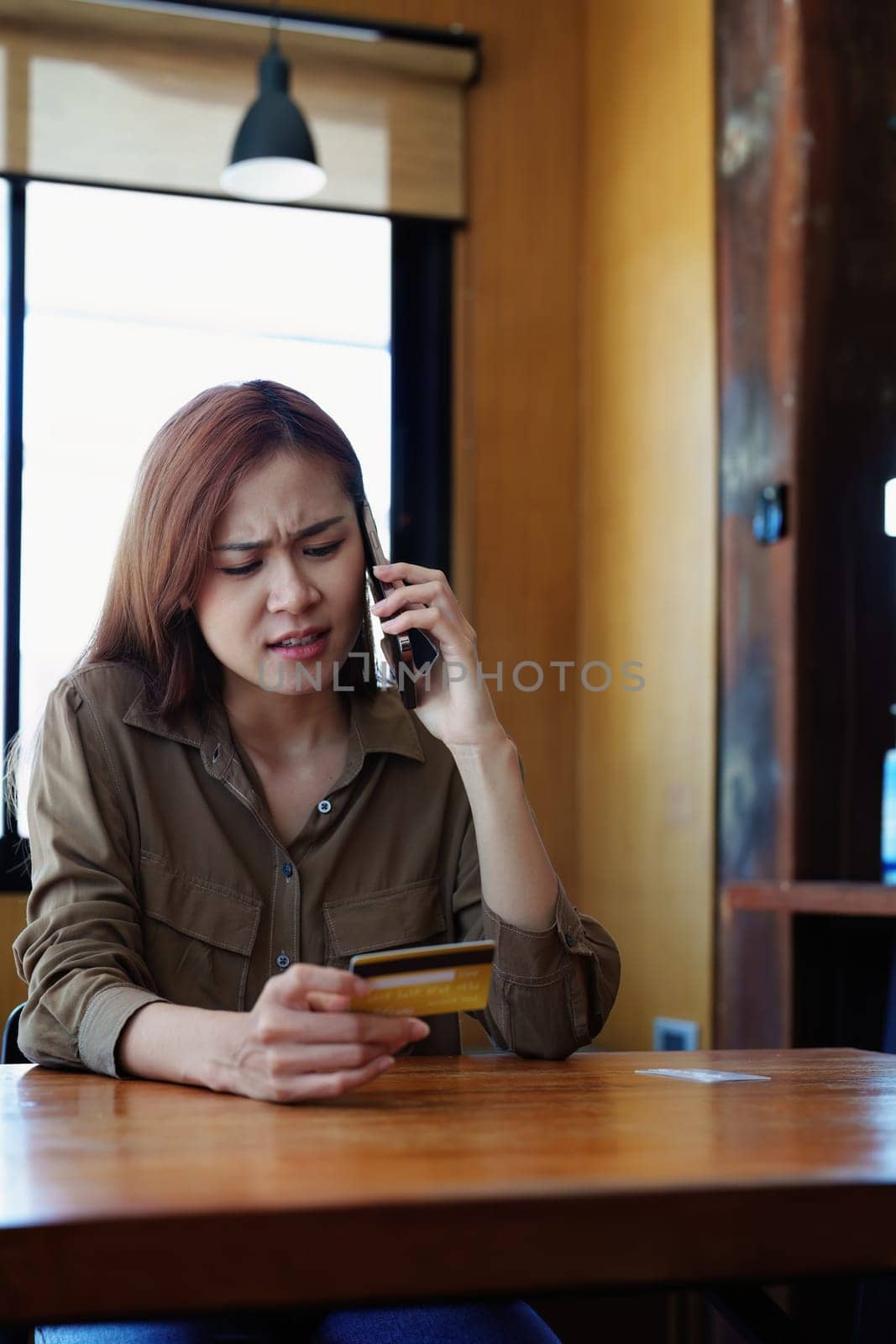 Portrait of a teenage Asian woman expressing dissatisfaction with her credit card being banned while using her phone for online shopping by Manastrong