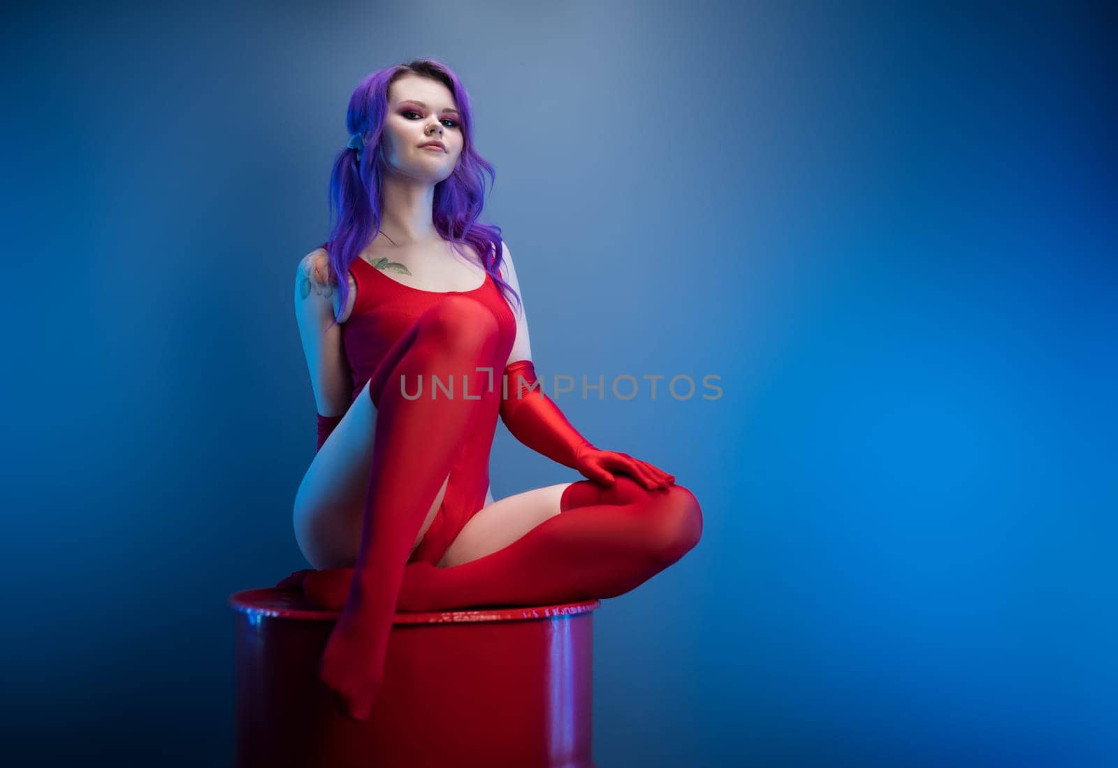 sexy girl in a red bodysuit, stockings and red gloves poses erotically on a blue background of copy paste