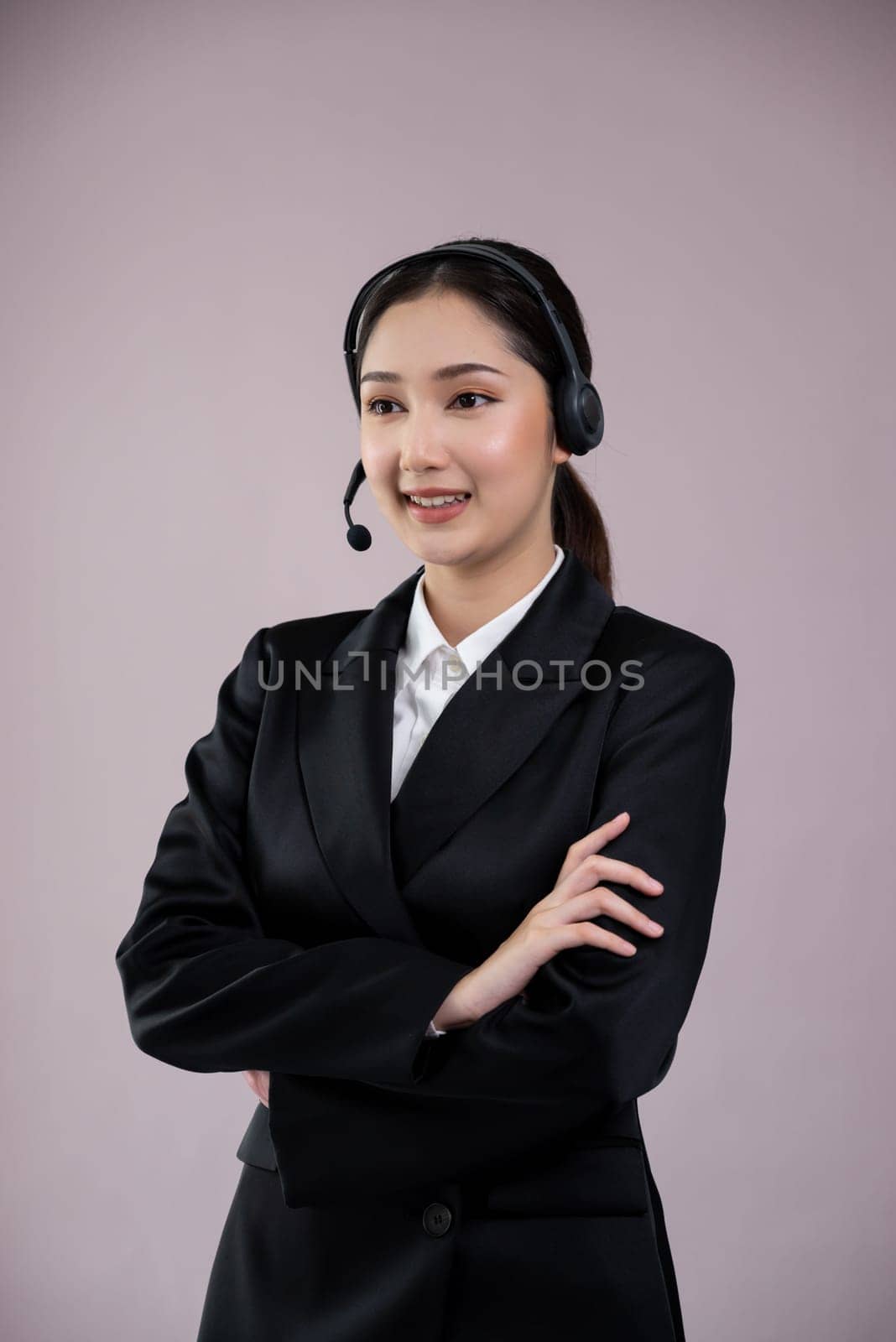 Attractive asian female call center operator with happy smile face advertises job opportunity on empty space, wearing a formal suit and headset on customizable isolated background. Enthusiastic