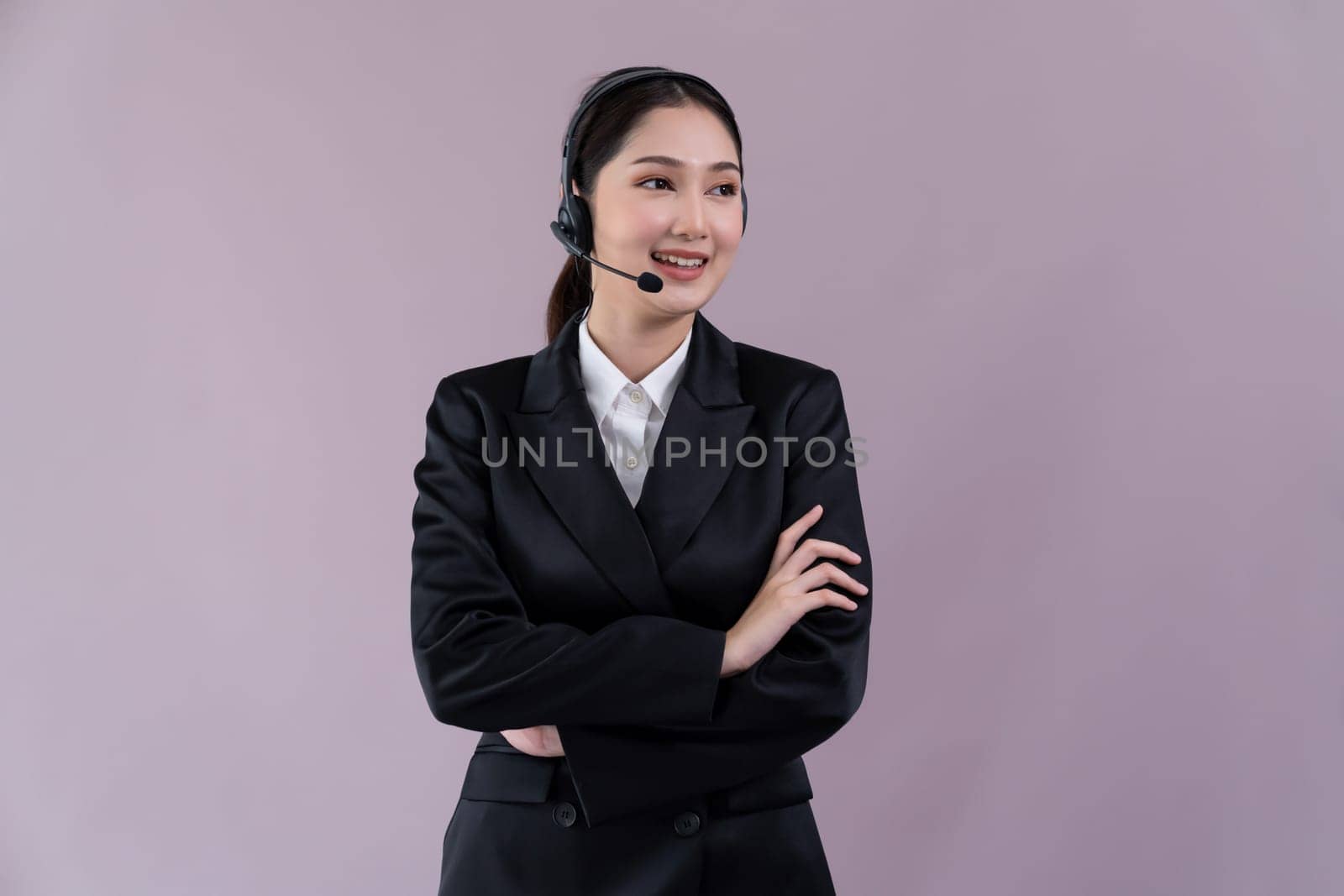 Attractive asian female call center operator with happy smile face advertises job opportunity on empty space, wearing a formal suit and headset on customizable isolated background. Enthusiastic