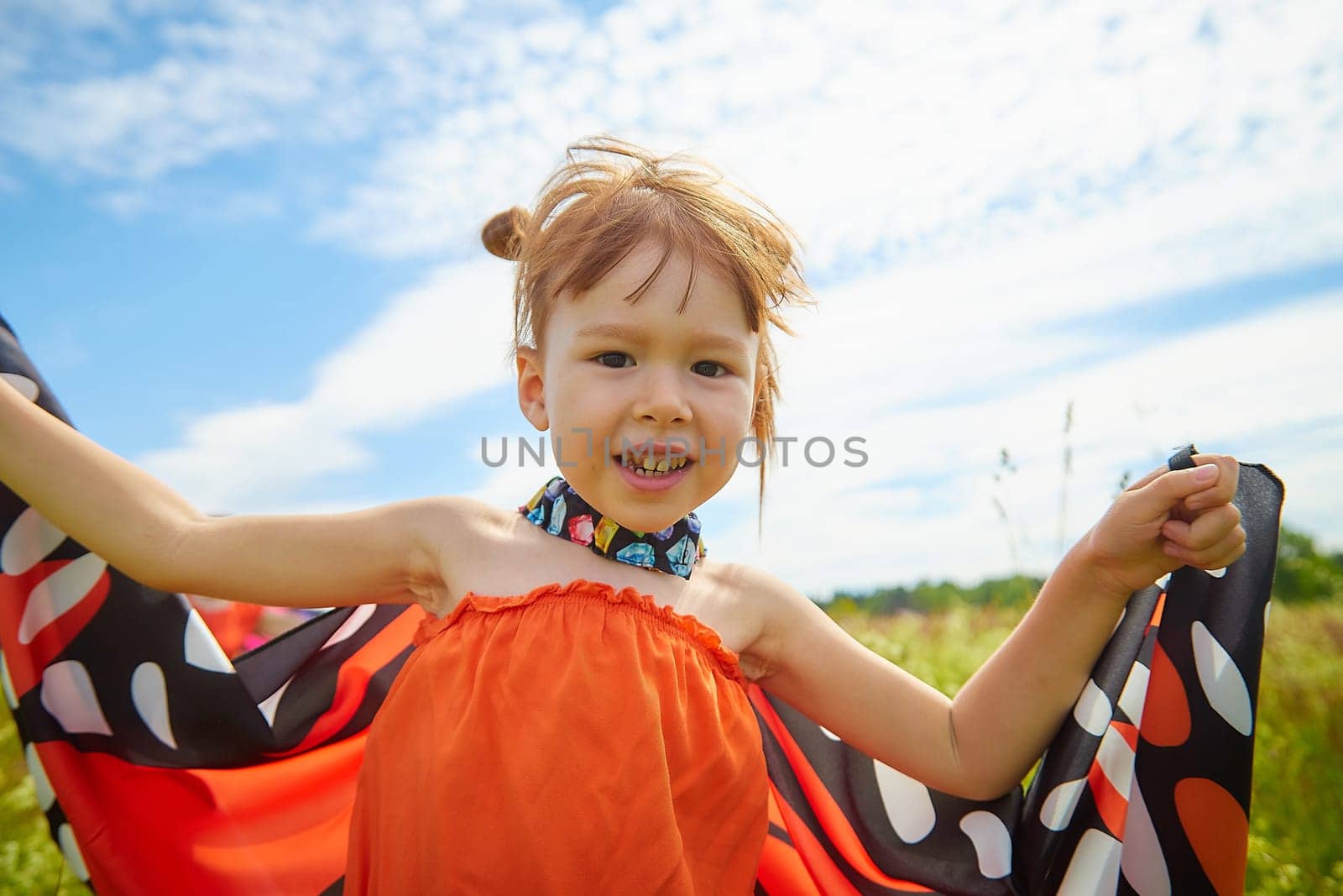 Portrait of little girl with Asian eyes and butterfly wings having fun and joy in meadow or field with grass and flowers on a sunny summer day by keleny