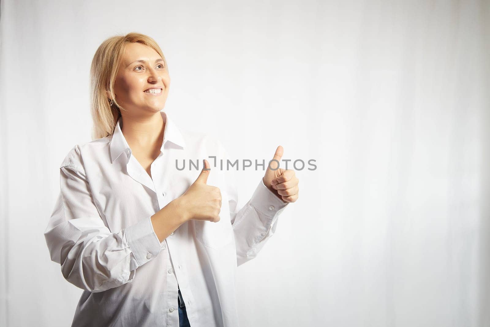 Portrait of a pretty blonde smiling woman posing on a white background. Happy girl model in white shirt in studio. Lady winner is joyfull. Copy space by keleny