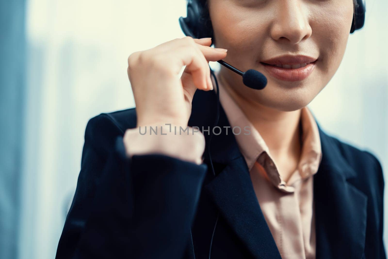 Asian call center with headset and microphone working on her workspace looking at camera. Female operator provide exceptional customer service. Supportive call center agent portrait. Enthusiastic