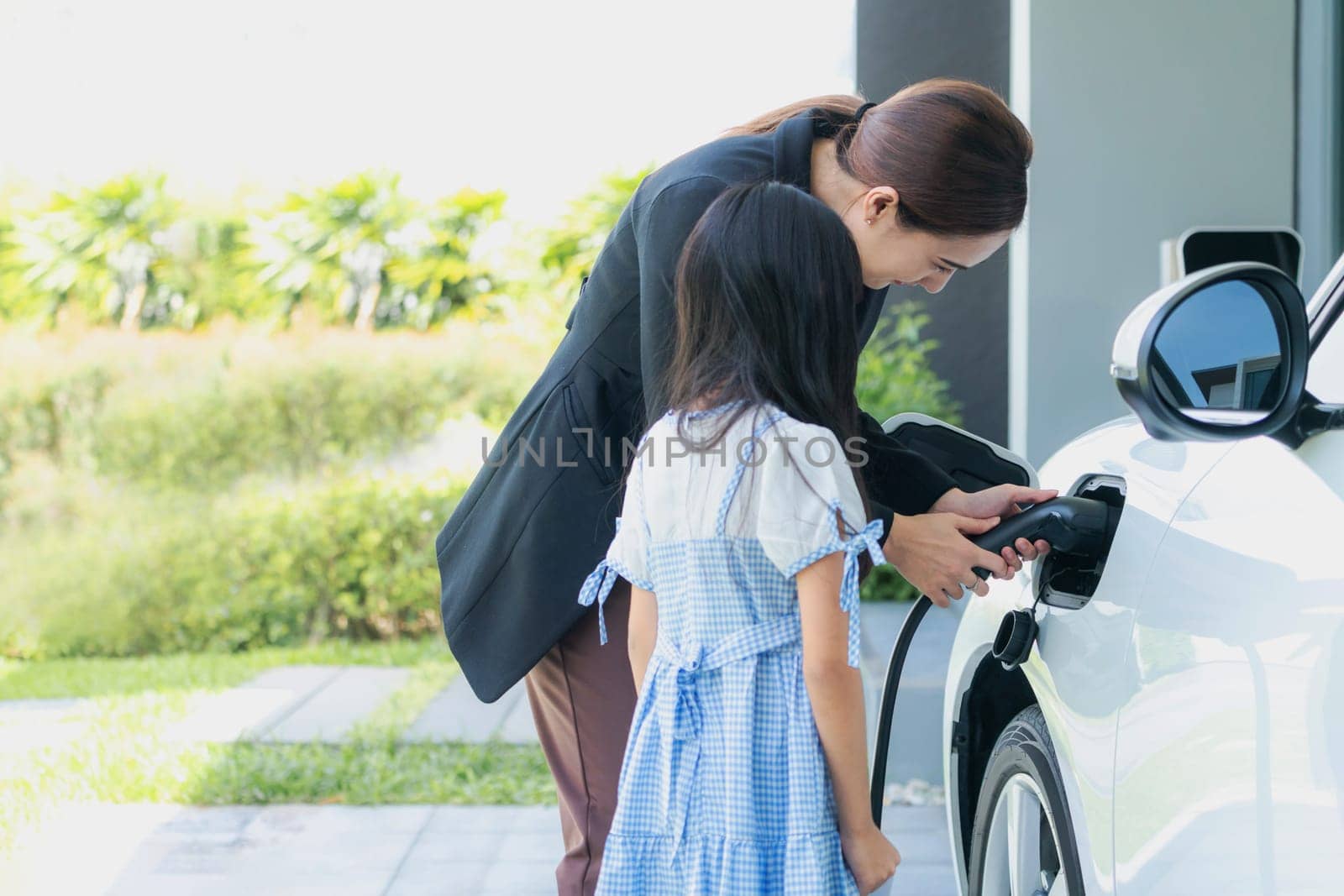 Progressive lifestyle of mother and daughter who have just returned from school in an electric vehicle that is being charged at home. Electric vehicle powered by sustainable clean energy.