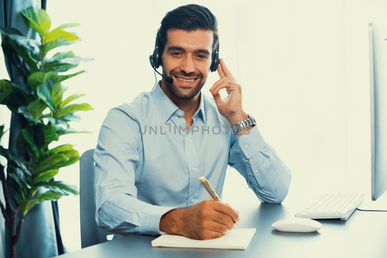Male call center operator or telesales representative siting at his office desk wearing headset portrait. Customer service agent with smiling to camera on workplace. fervent