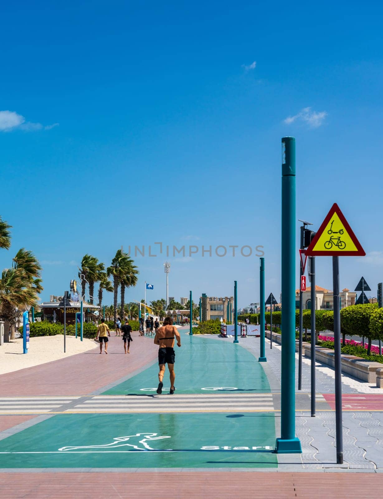 Dubai, UAE - 3 April 2023: Man jogging along green Zero Point running track at Jumeirah public beach