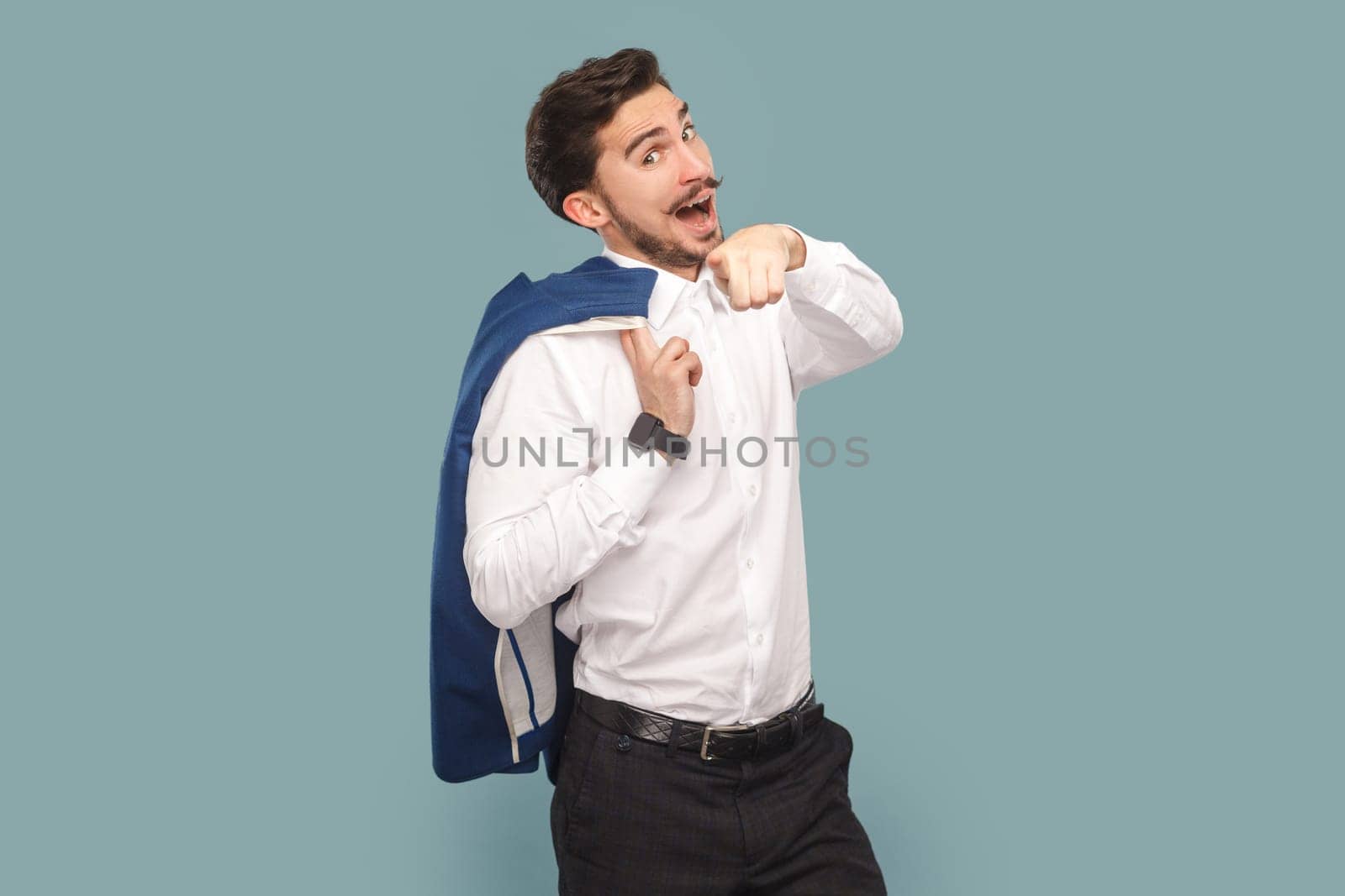 Portrait of amazed man with mustache standing pointing to camera, choosing you, flirting with attractive girl, wearing Indoor studio shot isolated on light blue background.