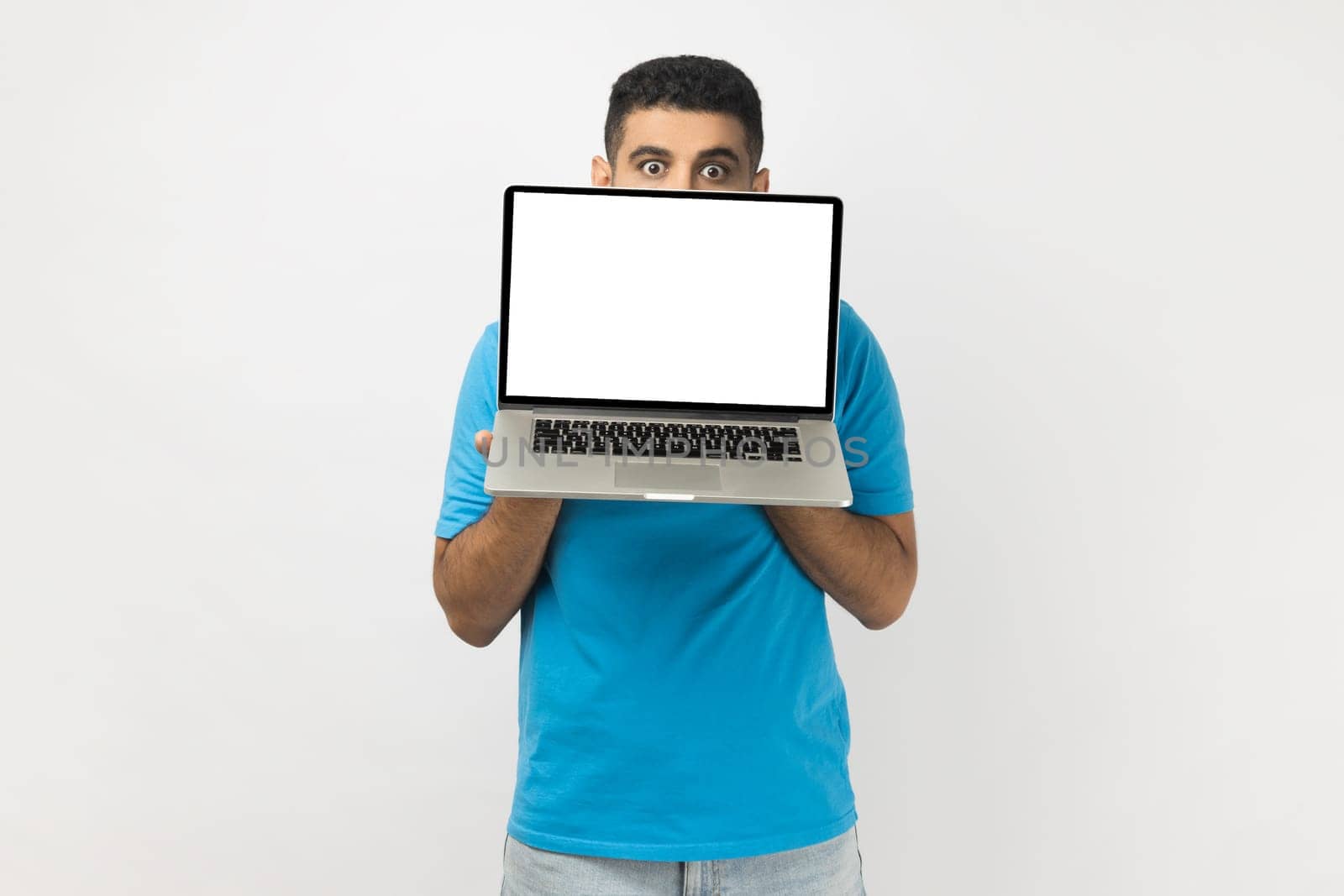 Shy young adult man hiding half of his face behind laptop with empty display, looking at camera. by Khosro1