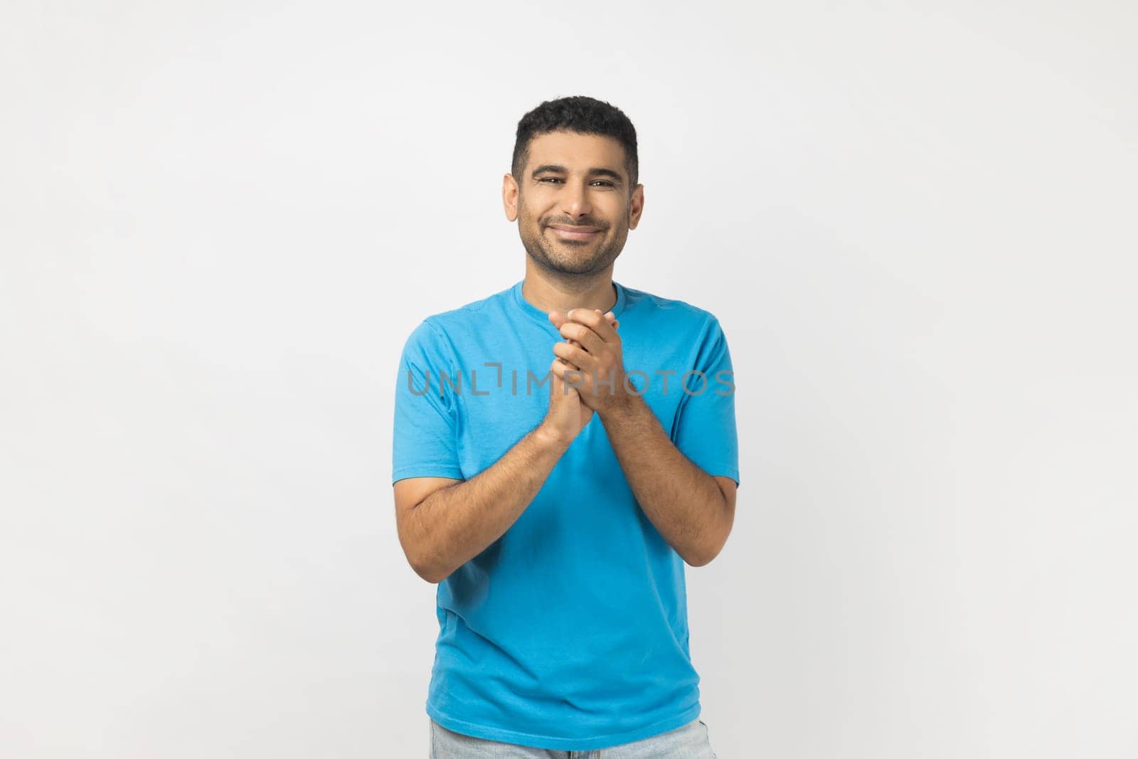 Portrait of positive optimistic smiling unshaven man wearing blue T- shirt standing applauding, being satisfied of performance, enjoying. Indoor studio shot isolated on gray background.