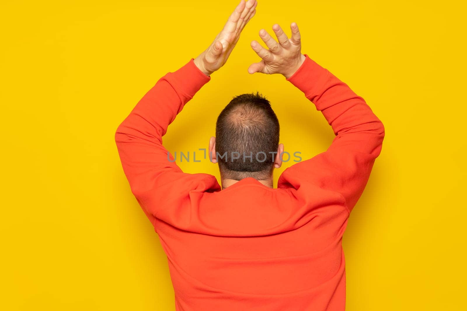 Half-bald man energetically clapping his back, he is excited about the spectacle he has just witnessed. Isolated on yellow background.