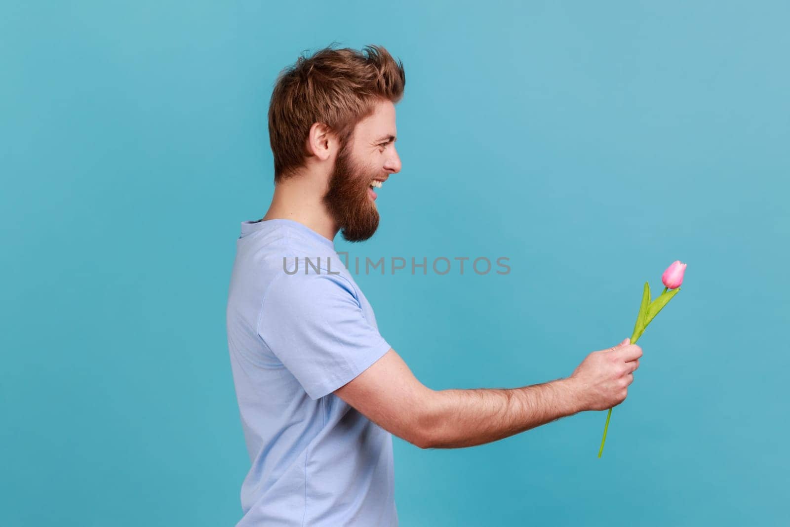 Man in blue T-shirt standing, holding and giving rose tulip flower and looking smiling ahead. by Khosro1