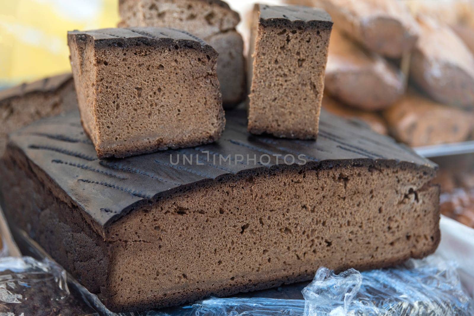 A loaf of black rye bread on the counter of a bakery is cut into pieces, close-up. Texture of black ecological bread. by SERSOL